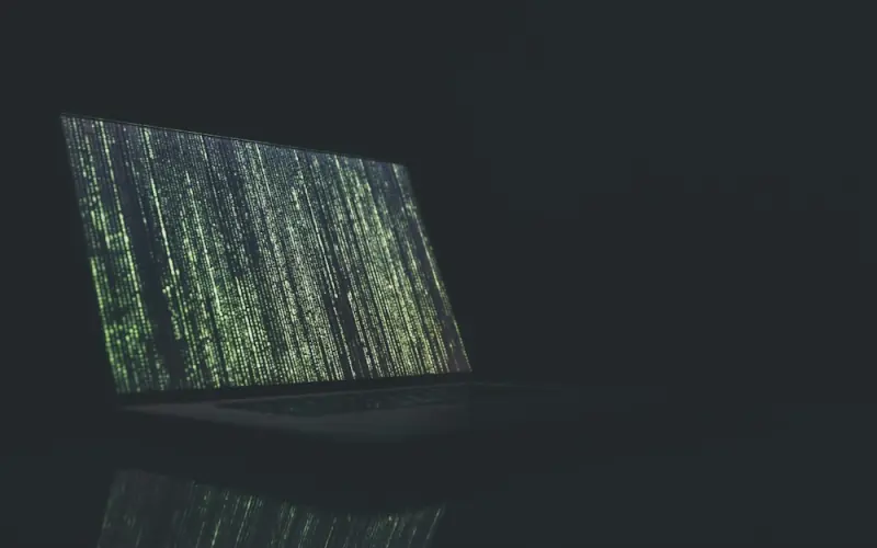 Laptop showing streams of code in a dark room
